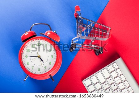 Red alarm clock, shopping trolley and keyboard on the doubble color background. Online shopping and sales concept