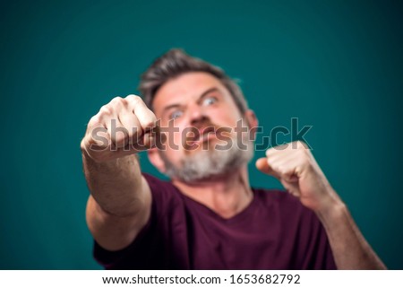 A portrait of bearded angry man in red t-shirt showing fist at camera. People and emotions concept
