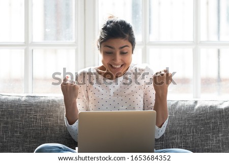 Indian woman in anticipation online lottery result holds fists together hopes for luck, girl holding pc on lap feeling excitement got loan opportunity from bank, sale big discount better offer concept Royalty-Free Stock Photo #1653684352