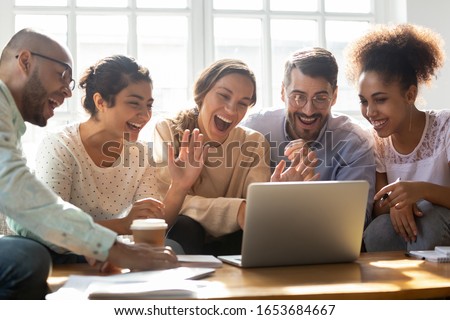 Five multi-ethnic millennial friends sitting on sofa looking at computer screen wave hands laughing enjoy distant communication with mate. Make videocall, greeting online by webcam modern tech concept Royalty-Free Stock Photo #1653684667