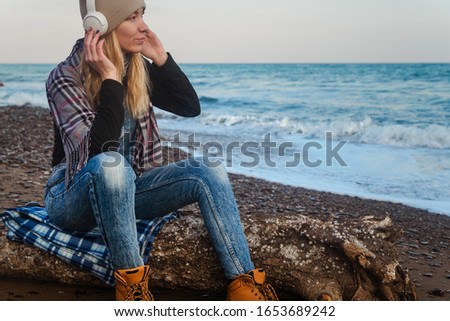 Girl on the seashore listens to music on headphones