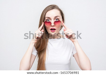 Shocked pretty woman in heart-shaped glasses, portrait, white background, close up