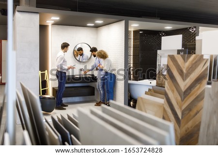 Two person spend time at interior decor store talking with seller manager about  tab bath or mirror trying to choose the right ones.