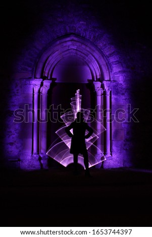 Silhouette of a woman in front of an arch carved in stone. Curved abstract shape made with a light saber violet. Lightpainting session at night. Leds light effect. Background for wallpaper.