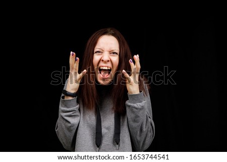 Middle age woman is angry. The girl wear casual sweeter on a black background. Evil woman, hands on her sides.
