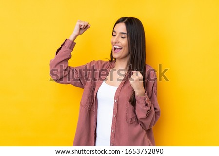 Young brunette woman over isolated yellow background celebrating a victory