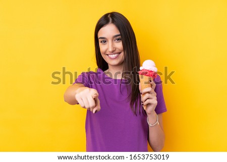 Young brunette woman with a cornet ice cream over isolated yellow background points finger at you with a confident expression