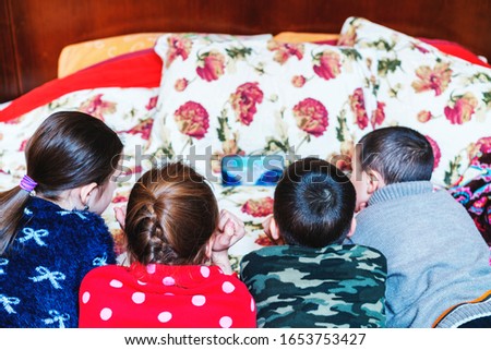 Four children in bed watching a cartoon on a smartphone. kids are watching cartoons on smartphone on the parent's bed. Primary school age girls andand boys spending time at home