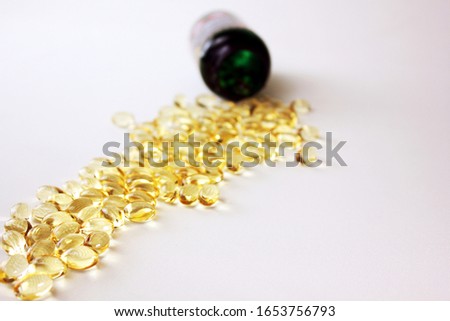 Fish oil capsules on white table and background with green / dark pill glass in the background. 