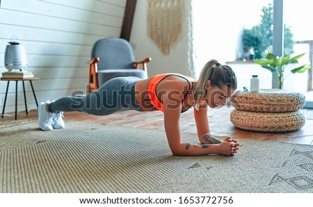 Young beautiful athletic girl in leggings and top makes an exercise plank. Healthy lifestyle. A woman goes in for sports at home. Royalty-Free Stock Photo #1653772756