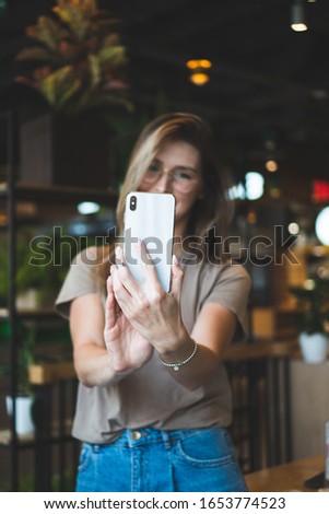 Smiling caucasian girl in a casual making selfie at cafe, beautiful young woman use phone