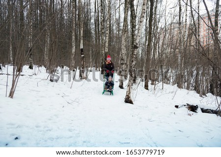 Cheerful kid on a sled. Winter holiday. A child in the winter forest.