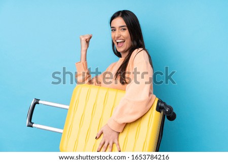Young brunette woman over isolated blue background in vacation with travel suitcase