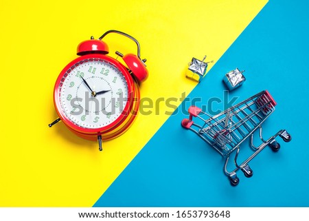 Red alarm clock, small shopping trolley on color background. Shopping concept