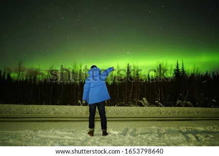 man showing Aurora Borealis with forest in the background