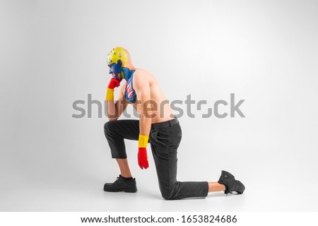 Strange man with makeup on his head and shoulder in white t-shirt, red and yellow gloves, red stands on his knee