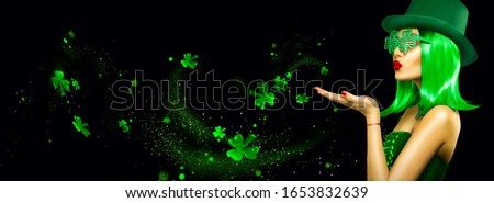 St. Patrick's Day leprechaun model girl pointing hand, holding product, isolated on black magic background, blowing shamrock leaves. Patrick Day pub party, celebrating. Border, Widescreen