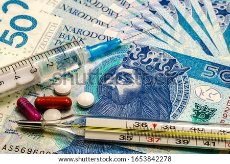 A syringe, thermometer, and pills on background made of polish 50 zl banknotes