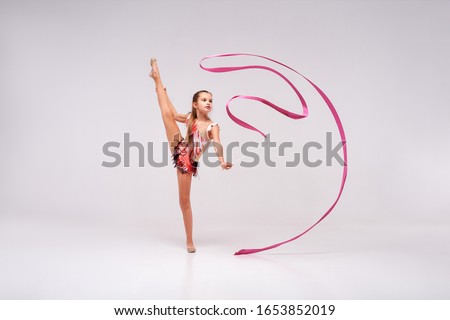 Flexible cute little girl child gymnast doing acrobatic exercise using ribbon isolated on a white background. Sport, training, fitness, active lifestyle concept. Horizontal shot