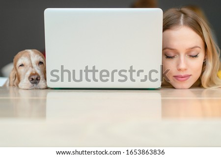 Closeup portrait of blonde woman head and head of her cocker spaniel dog lying togther on a table along the edges of laptop