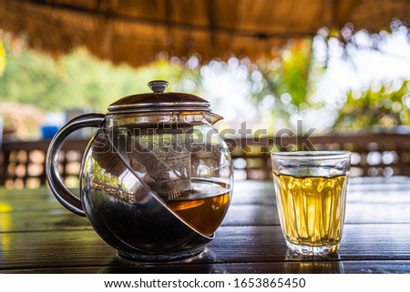 Beautiful warm picture of transparent teapot kettle with tasty green black tea with apple, lemon and ginger on a table.