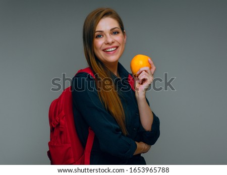 Student girl in black dress with red backpack holding whole orange. isolated studio portrait.