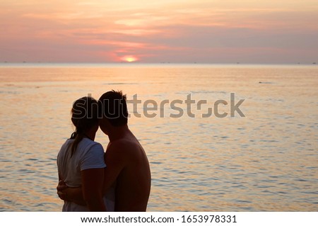   The married couple looks at the dying sunset on the seashore                             