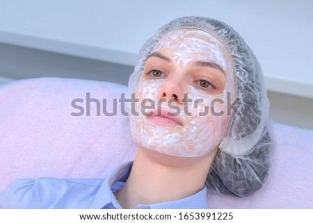 Woman with anesthetic cream on face skin before biorevitalization for numbing, portrait closeup. Beauty procedure in cosmetology clinic. Young woman is waiting for anesthesia to take effect.
