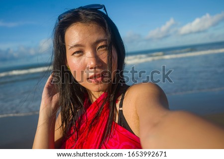 young happy and attractive Asian Korean woman in sarong taking selfie photo for social media with mobile phone enjoying Summer holidays at tropical beach in vacations and lifestyle concept