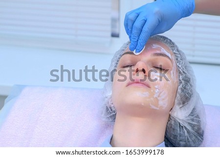 Beautician wiping cream with anesthetic cotton pads from girl face before biorevitalization in cosmetology. Cosmetologist preparing girl for mesotherapy procedure in beauty clinic, portrait closeup.