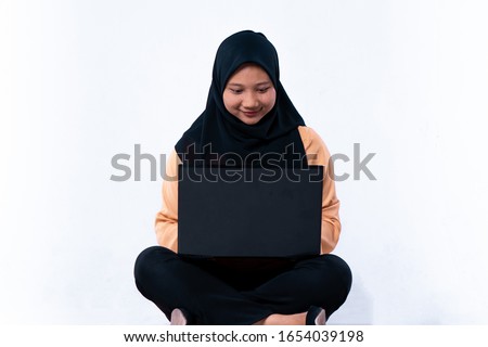 Smiling asian woman typing on laptop computer while sitting on the floor with legs crossed isolated over white background