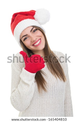 Positive young Caucasian brunette woman showing thumb up wearing Christmas Santa beanie hat smiling looking at camera isolated on white background.
