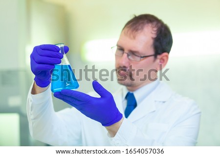A scientist holds and studies a flask with blue liquid in a scientific laboratory