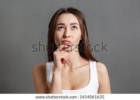 The concept of searching for ideas and information. Portrait of a pensive young Caucasian woman looking up. Gray background. Copy space