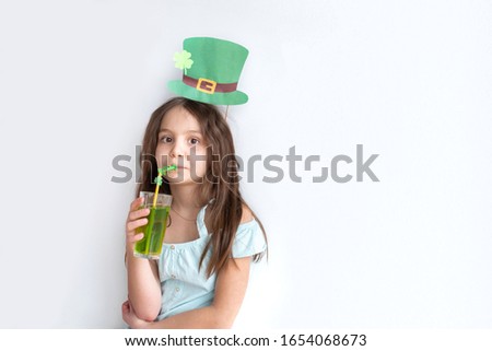Closeup portrait of a pretty preteen caucasian girl in an emerald leprechaun hat with glass of green drink with a straw decorated with clover. St. Patrick's Day holiday concept