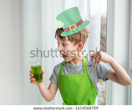 St Patrick's Day holiday concept. Joyful emotional caucasian boy with green paper leprechaun hat with clover and glass of green drink on white background.