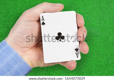 Deck of playing cards in a male hand with ace of clubs face-up on a blurred background of green game table 
