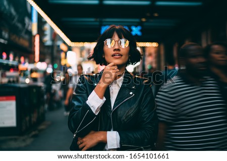 Youthful female traveller in stylish spectacles for vision correction spending time for walking around metropolitan downtown and explore New York nightlife on leisure, young woman in streetwear Royalty-Free Stock Photo #1654101661