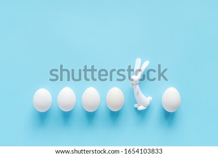 Row white eggs and bunny rabbit figurine on blue background with copy space. Happy easter, Not like everyone else concept. Creative Flat lay Top view. Template for greeting card, invitation, postcard.