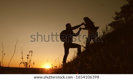 Travelers descend from mountain at sunset, hold hands. adventure and travel concept. teamwork of business people. Hiker man holds out his hand to woman traveler descending from top of hill.
