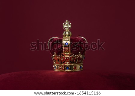 Golden crown on a velvet cushion on a deep red background with copy space Royalty-Free Stock Photo #1654115116