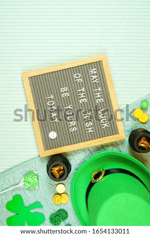 St Patrick's Day hygge style creative composition flat lay layout with leprechaun hat, chocolate coins, shamrocks and candy with letter board in bed, with negative copy space.