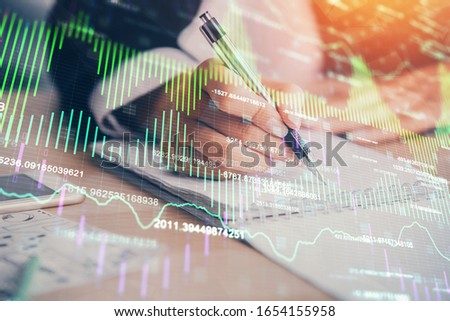 A woman hands writing information about stock market in notepad. Forex chart holograms in front. Concept of research. Multi exposure