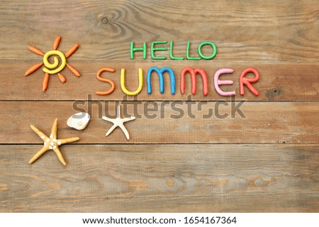inscription "hello summer" made from plasticine of different colors on a wooden surface