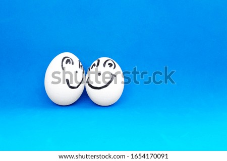 Two chicken eggs with smiling and cheerful faces on a blue background.
