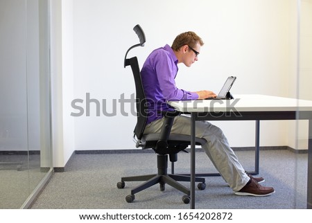 text neck - man in slouching position on ergonomic chair working with tablet at desk Royalty-Free Stock Photo #1654202872