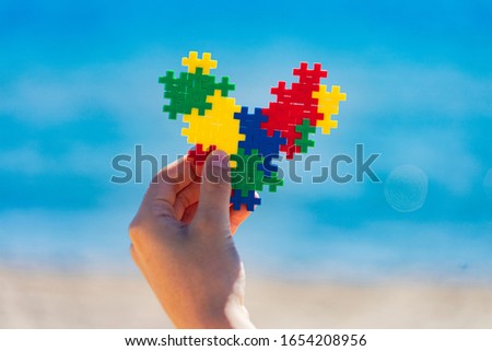 Autism friendly holidays. Child hands holding colorful heart with sea ocean sandy beach background