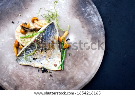 Gourmet fried gilthead fish filet with sliced dumpling, glasswort and algae as top view on a modern design plate with copy space right
