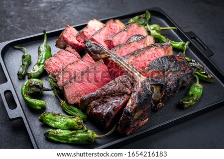 Barbecue dry aged wagyu porterhouse beef steak sliced with large fillet piece with hot chili as closeup on a modern design black cast iron tray  Royalty-Free Stock Photo #1654216183