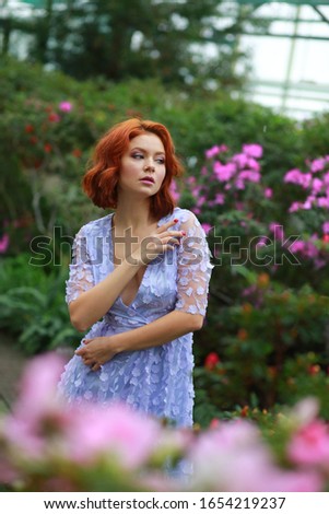 beautiful red-haired girl in arranger where azalea blooms in a colorful flying dress